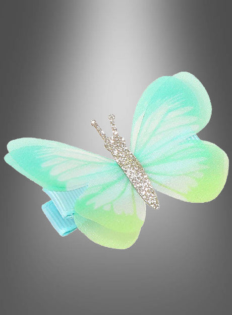 Eine Haarspange „Schmetterling mit Glitzer“ in Blau und Grün, verziert mit funkelnden silbernen Akzenten, die an zarte Schmetterlingsflügel erinnern, wird vor einem grauen Hintergrund mit Farbverlauf präsentiert. Dieses elegante Haaraccessoire verleiht jeder Frisur eine verspielte Note.