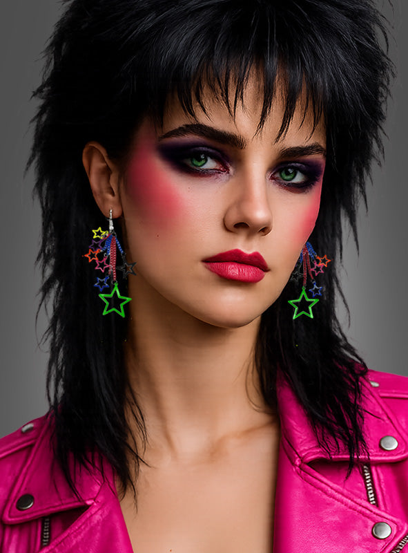 Eine Frau mit auffälligem Make-up im Stil der 1980er Jahre, die große Ohrringe im Stil der 80er Jahre – Sterne, Clips oder Haken – sowie eine knallpinke Kunstlederjacke trägt, posiert vor einem schlichten grauen Hintergrund und sorgt so für einen markanten, retro-inspirierten Look.
