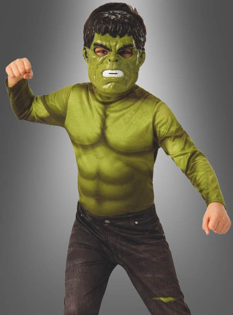 Ein Kind, das ein Hulk-Endgame-Kostüm für Kinder und eine Maske trägt, reckt vor einem grauen Hintergrund mit Farbverlauf in einer kraftvollen Pose die Fäuste in die Höhe.