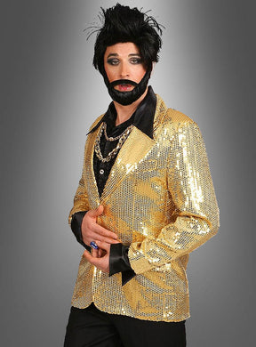 Eine Person, die eine glänzende goldene Paillettenjacke für Herren, ein schwarzes Hemd, mehrere Halsketten, einen künstlichen Bart und eine gestylte schwarze Perücke trägt, steht vor einem grauen Hintergrund mit Farbverlauf – ein auffälliges Karnevalsoutfit, das alle Blicke auf sich zieht.