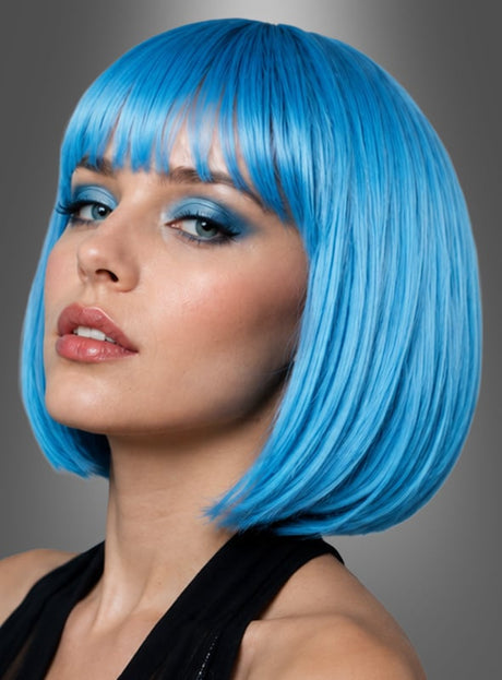 Eine Frau mit kurzen, glatten, leuchtend blauen Haaren und einem Pony, gestylt mit der Perücke „Bobfrisur Helene Blau Lila Grün“, die blauen Lidschatten und ein schwarzes Oberteil trägt, blickt vor einem grauen Hintergrund in die Kamera.
