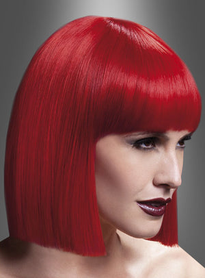 Eine Person, die die „Lola Perücke Deluxe Pagenschnitt rot“ trägt – einen glatten, leuchtend roten Bob, der an einen klassischen Pagenschnitt erinnert –, blickt zur Seite. Der Hintergrund weist einen Farbverlauf von Dunkel- nach Hellgrau auf, der an den ikonischen Stil eines Kostüms aus den 20er Jahren erinnert.