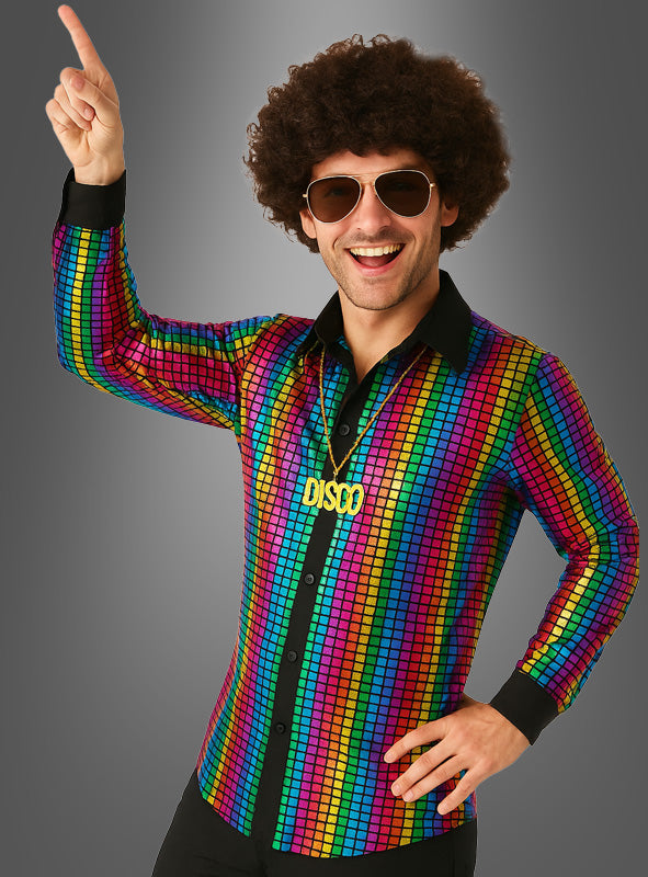 Ein Mann, der das „Rainbow Disco Set mit Hemd für Männer“ trägt – mit seinem leuchtenden Hemd im Regenbogenmuster –, dazu eine übergroße Sonnenbrille und eine DISCO-Halskette, lächelt und zeigt mit einem Finger nach oben vor einem grauen Hintergrund.