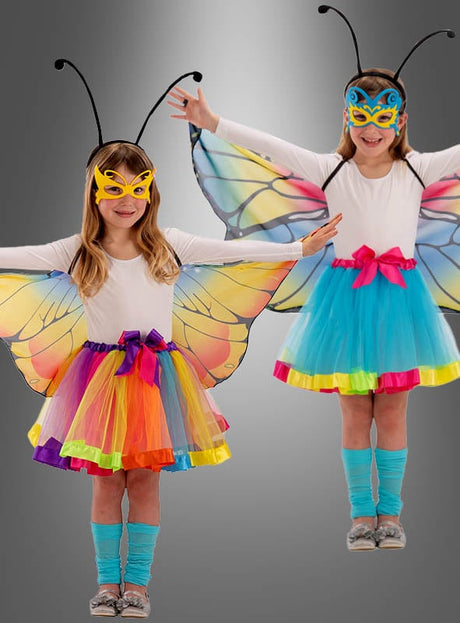 Zwei kleine Mädchen tragen das farbenfrohe „Schmetterling Flügel“-Verkleidungsset mit leuchtenden Schmetterlingsflügeln, passenden Masken, blauen Röcken und blauen Socken, während sie mit ausgestreckten Armen vor einem grauen Hintergrund mit Farbverlauf posieren – ein ideales Geschenk für Mädchen, die sich gerne verkleiden und fantasievoll spielen.