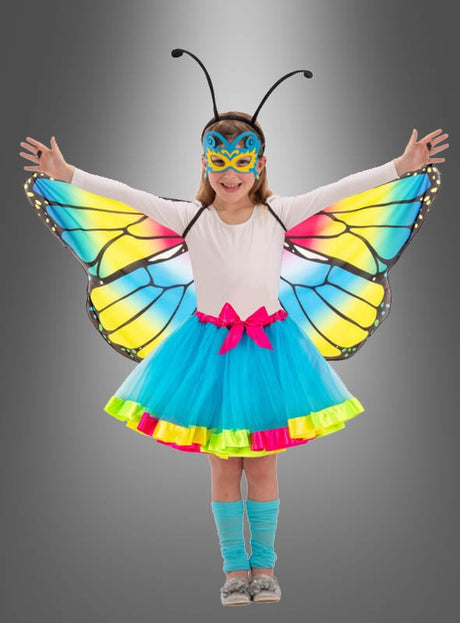 Ein Kind, das das „Schmetterling Flügel“-Kostüm trägt – bestehend aus farbenfrohen Flügeln, einem blauen Rock, einer Maske und einem Stirnband mit Fühlern –, steht mit ausgestreckten Armen vor einem grauen Hintergrund und ist damit das perfekte Geschenk für Mädchen, die gerne fantasievoll spielen.