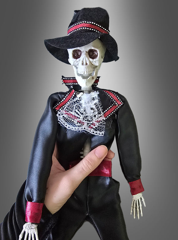 Eine Hand hält eine „Tag der Toten“-Voodoo-Puppe (42 cm, Bräutigam), die einen schwarzen Anzug, einen schwarzen Hut und rote Akzente trägt und vor einem grau verlaufenden Hintergrund den Geist des mexikanischen Halloween heraufbeschwört.