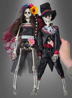 Zwei „Tag der Toten Voodoo-Puppen 42 cm Braut oder Bräutigam“ in farbenfroher traditioneller Tracht – die eine als Braut mit Blumen, die andere als Bräutigam in Anzug und Zylinder – sind vor einem grauen Hintergrund ausgestellt und eignen sich somit perfekt als Skelett-Brautpaar oder „Tag der Toten“-Dekoration für Ihre mexikanische Halloween-Feier.