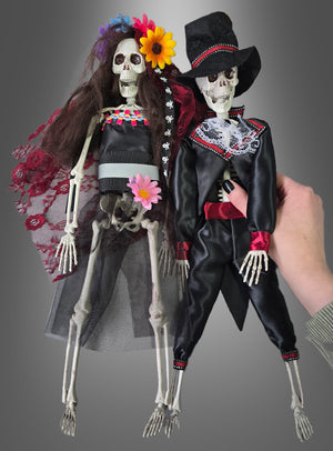 Zwei „Tag der Toten Voodoo-Puppen 42 cm Braut oder Bräutigam“ in farbenfroher traditioneller Tracht – die eine als Braut mit Blumen, die andere als Bräutigam in Anzug und Zylinder – sind vor einem grauen Hintergrund ausgestellt und eignen sich somit perfekt als Skelett-Brautpaar oder „Tag der Toten“-Dekoration für Ihre mexikanische Halloween-Feier.