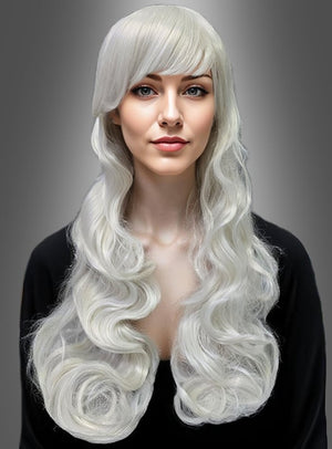 Eine Frau mit langen, welligen, platinblonden Haaren und einem geraden Pony, die ein schwarzes Oberteil trägt, posiert vor einem schlichten grauen Hintergrund – ihr atemberaubender Look wird durch die Langhaar-Lockenperücke „Lady Godiva“ abgerundet, die für zusätzliches Volumen und Glamour sorgt und sich perfekt für jedes Karnevalskostüm oder jeden besonderen Anlass eignet.
