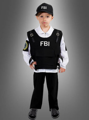 Ein kleines Kind steht vor einem grau abgestuften Hintergrund und trägt ein FBI-Agenten-Kostüm für Kinder, komplett mit Mütze, Weste und weißem Hemd.
