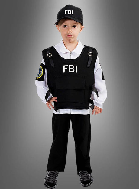 Ein kleines Kind steht vor einem grau abgestuften Hintergrund und trägt ein FBI-Agenten-Kostüm für Kinder, komplett mit Mütze, Weste und weißem Hemd.