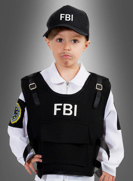 Ein kleines Kind mit einer FBI-Kappe, einem weißen Hemd und einer schwarzen Einsatzweste mit FBI-Aufdruck steht vor einem grauen Hintergrund mit Farbverlauf – die ideale Wahl für alle, die auf der Suche nach einem authentischen FBI-Agenten-Kostüm für Kinder sind.