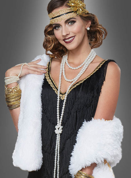 Eine Frau in einem Flapper-Kostüm im Stil der 1920er Jahre, bestehend aus einem schwarzen Kleid, Perlenketten, einem goldenen Stirnband und goldenen Armreifen, elegant drapiert mit der weißen „Lange Stola 20er Jahre“ als raffiniertes Accessoire, posiert vor einem grauen Hintergrund mit Farbverlauf.