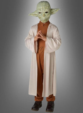 Ein Kind im Yoda-Kinderkostüm „Original STAR WARS“ – mit einer Yoda-Maske, einem braunen Outfit und einer langen beigen Robe – steht mit gefalteten Händen vor einem grauen Hintergrund und ist damit ideal für Fans, die ein authentisches STAR WARS-Kostüm suchen.
