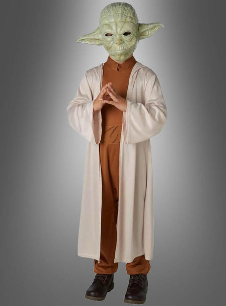Ein Kind im Yoda-Kinderkostüm „Original STAR WARS“ – mit einer Yoda-Maske, einem braunen Outfit und einer langen beigen Robe – steht mit gefalteten Händen vor einem grauen Hintergrund und ist damit ideal für Fans, die ein authentisches STAR WARS-Kostüm suchen.