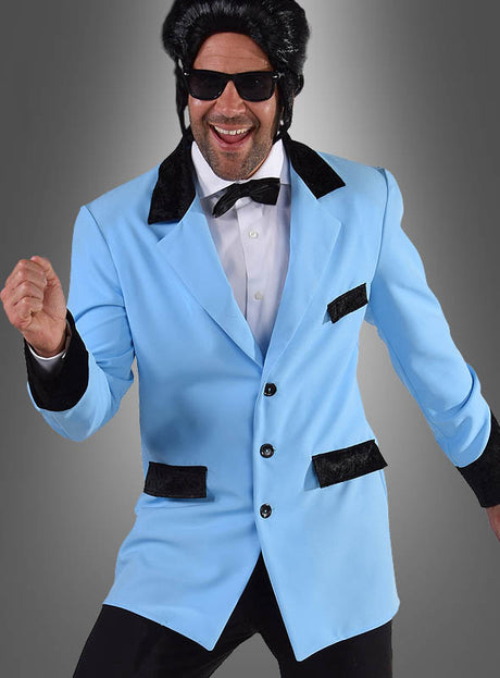 Ein Mann, der eine hellblaue Ted-Jacke im Stil der 50er Jahre mit schwarzen Akzenten trägt, dazu ein weißes Hemd, eine schwarze Fliege, eine dunkle Sonnenbrille und eine schwarze Perücke, lächelt und nimmt vor einem grauen Hintergrund eine verspielte Pose ein – ein perfekter Look für jede Kostüm-Mottoparty im Stil der 50er Jahre.