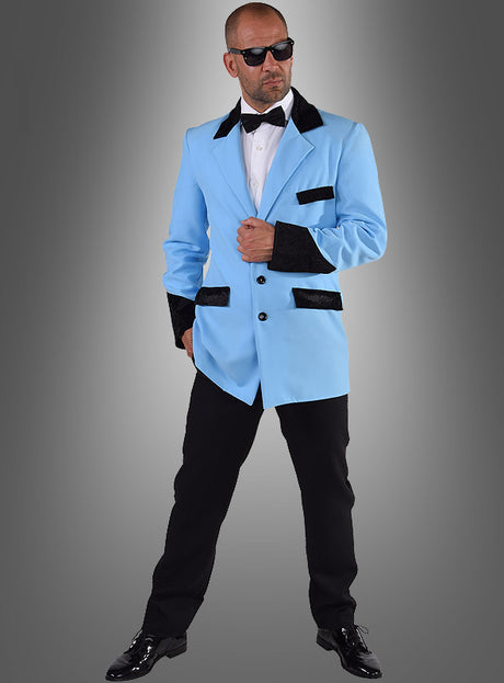 Ein Mann mit Sonnenbrille, einer blauen Ted-Jacke im Stil der 50er Jahre mit schwarzen Akzenten, einem weißen Hemd, einer schwarzen Fliege, einer schwarzen Hose und schwarzen Schuhen, der vor einem grauen Hintergrund mit Farbverlauf steht – perfekt für jede Mottoparty oder als authentisches Kostüm im Stil der 50er Jahre.