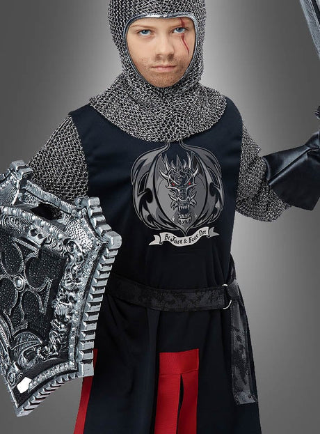 Eine Figur in mittelalterlicher Ritterrüstung hält Schild und Schwert in den Händen und trägt eine Tunika mit einem Drachenwappen und der Aufschrift „Protect & Knight“ vor einem schlichten grauen Hintergrund. Das Ritterkostüm für Kinder eignet sich perfekt als Faschingkostüm für Kinder oder Ritterverkleidung für Kinder und weckt den Abenteuergeist jedes jungen Helden.
