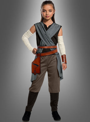Ein junges Mädchen trägt das Rey-Kostüm für Kinder aus „Star Wars VIII“ – bestehend aus grauen und braunen Gewändern, einer braunen Hose, Armwickeln, braunen Stiefeln und einem Holster – und steht vor einem grauen Hintergrund. Dieses authentische Jedi-Kostüm ist das perfekte Kinderkostüm für jeden jungen „Star Wars“-Fan.