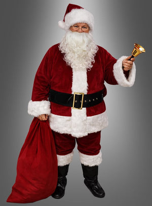 Eine Person, die ein waschbares Weihnachtsmannkostüm mit Bart und Perücke trägt, steht vor einem grauen Hintergrund und hält in der einen Hand eine goldene Glocke und in der anderen einen großen roten Sack.