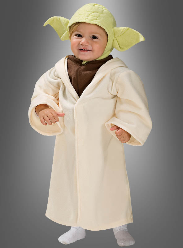Ein kleines Kind, das das originale STAR WARS-Kinderkostüm von Yoda trägt – bestehend aus einem grünen Hut und einer cremefarbenen Robe –, steht vor einem grauen Hintergrund.