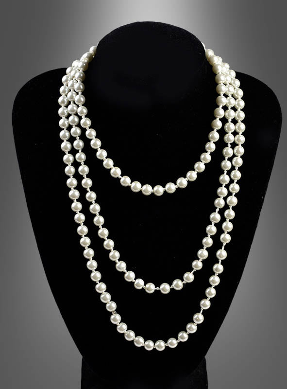 Auf einem schwarzen Ausstellungsständer wird die „Deluxe Perlenkette Modeschmuck creme“ präsentiert, eine dreisträngige Halskette mit runden, weißen Perlen, die vor einem grauen Hintergrund mit Farbverlauf zur Geltung kommt.