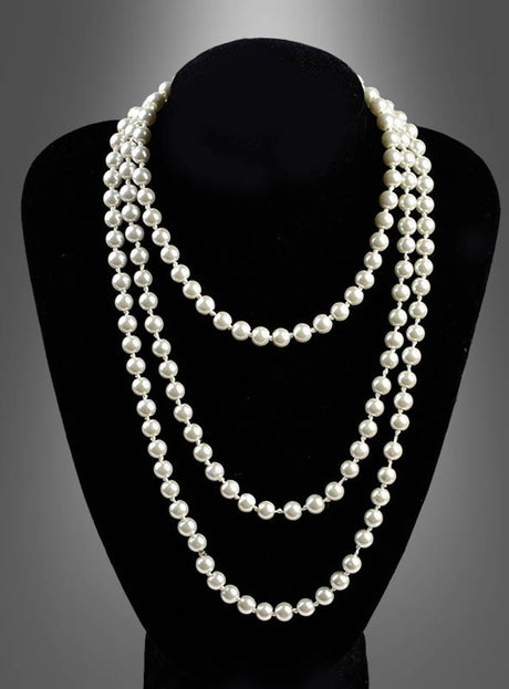 Auf einem schwarzen Ausstellungsständer wird die „Deluxe Perlenkette Modeschmuck creme“ präsentiert, eine dreisträngige Halskette mit runden, weißen Perlen, die vor einem grauen Hintergrund mit Farbverlauf zur Geltung kommt.