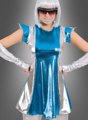 Eine Person trägt das schimmernde „Space Girl“-Weltraumkleid in Blau-Silber mit galaktischem Glanz, dazu passende Handschuhe, eine weiße Perücke, blauen Lippenstift und eine große dunkle Sonnenbrille und steht mit in die Hüften gestemten Händen vor einem grauen Hintergrund.
