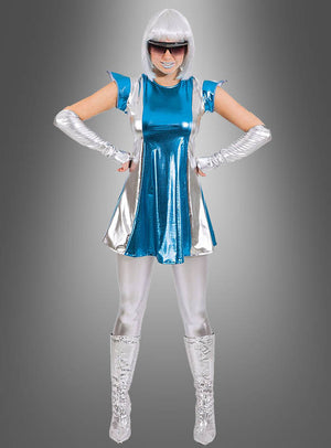 Eine Person in einem futuristischen Outfit in Metallic-Blau und Silber, bestehend aus dem „Schimmerndes Space Girl Weltall Kleid“, kombiniert mit schimmernden silbernen Leggings, Stiefeln, Handschuhen, einer weißen Perücke und einer dunklen Sonnenbrille. Mit den Händen in die Hüften gestemmt strahlt sie vor einem grauen Hintergrund mit Farbverlauf galaktischen Glanz aus.
