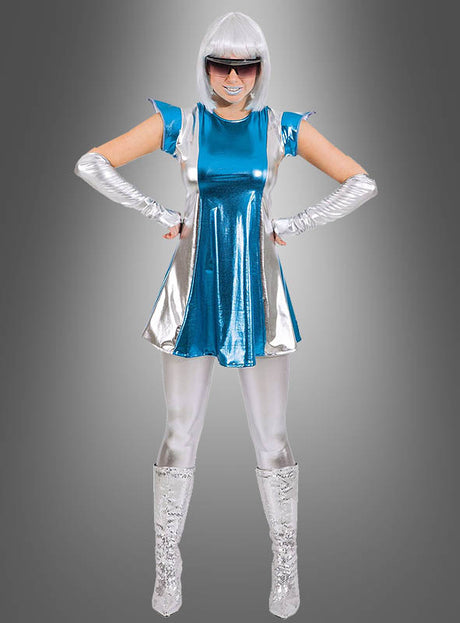 Eine Person in einem futuristischen Outfit in Metallic-Blau und Silber, bestehend aus dem „Schimmerndes Space Girl Weltall Kleid“, kombiniert mit schimmernden silbernen Leggings, Stiefeln, Handschuhen, einer weißen Perücke und einer dunklen Sonnenbrille. Mit den Händen in die Hüften gestemmt strahlt sie vor einem grauen Hintergrund mit Farbverlauf galaktischen Glanz aus.