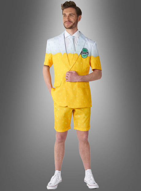 Ein Mann im „Sommerlicher Bieranzug“ – einem gelb-weißen Outfit mit Shorts, die einem Bierglas nachempfunden sind – steht vor einem grauen Hintergrund mit Farbverlauf und präsentiert damit das perfekte Sommeroutfit für jeden Bierliebhaber.