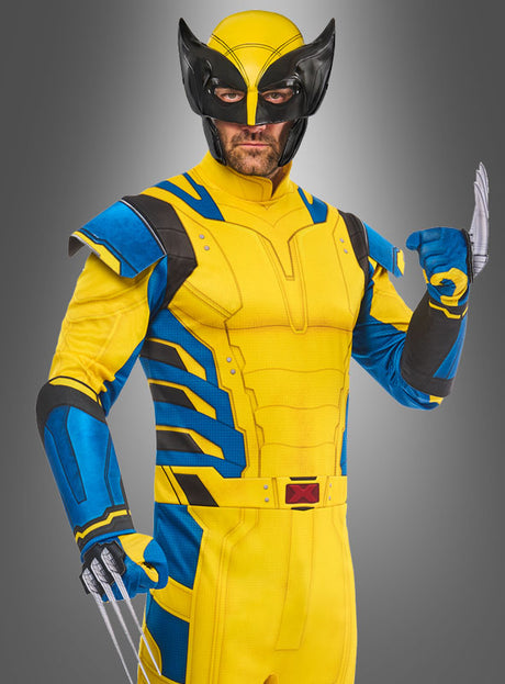 Eine Person im Wolverine-Kostüm für Herren – einem dynamischen gelb-blauen Superhelden-Outfit mit schwarzer Maske und Metallklauen – nimmt vor einem grauen Hintergrund mit Farbverlauf eine Pose ein und verkörpert damit den legendären Look der ikonischen Marvel-Kostümdesigns.