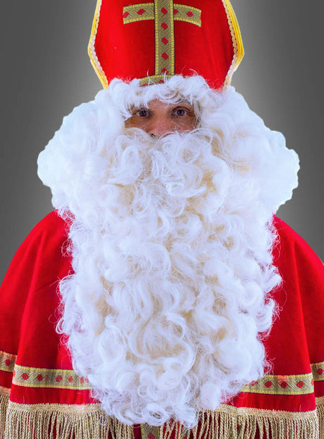 Eine als Nikolaus verkleidete Person, die eine rote Mütze und eine rote Robe mit goldenen Verzierungen trägt sowie den „Deluxe Bischof Nikolaus Bart und Perücke“, posiert vor einem grauen Hintergrund.