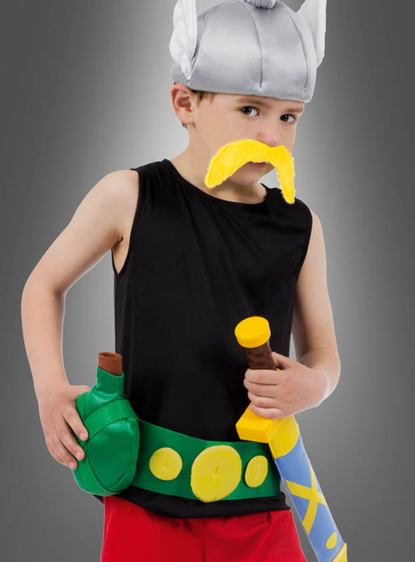 Ein Kind, das das „Deluxe Asterix Kinderkostüm Original“ trägt – bestehend aus einem silbernen Hörnerhelm, einem gelben Schnurrbart, einem schwarzen, ärmellosen Hemd, einer roten Hose sowie einem Spielzeugschwert mit Gürtel und Taschen –, posiert mit ernstem Gesichtsausdruck vor einem grauen Hintergrund und ist damit die perfekte Wahl für jeden Fan, der ein authentisches Kostüm sucht.