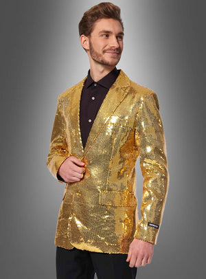 Ein Mann, der die „Pailletten Jackett Herren Gold“ über einem schwarzen Hemd trägt, steht vor einem schlichten grauen Hintergrund mit Farbverlauf, blickt leicht zur Seite und lächelt.