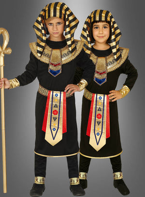 Zwei Kinder tragen passende Pharao-Kostüme für Kinder in Schwarz und Gold, jeweils mit gestreiften Kopfbedeckungen, verzierten Kragen und geschmückten Schärpen, während sie vor einem grauen Hintergrund stehen.
