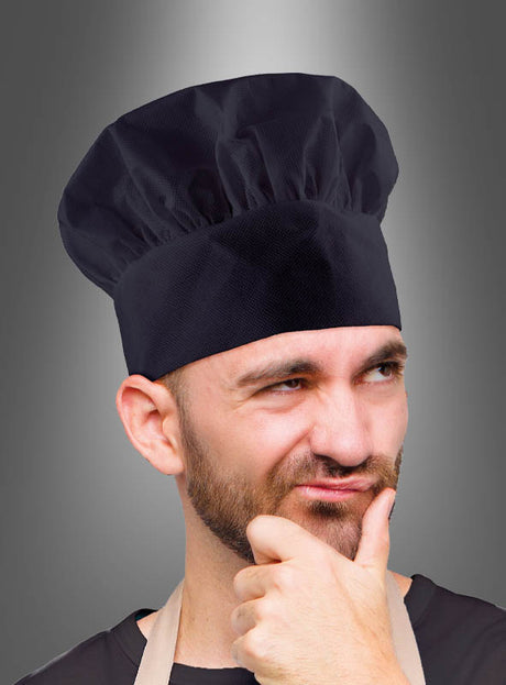Ein Mann, der eine Kochmütze für Erwachsene und eine Schürze trägt, steht vor einem grauen Hintergrund und blickt nachdenklich zur Seite, während er die Hand am Kinn hat – ein perfektes Küchenchef-Accessoire für alle, die ihr Kochkostüm vervollständigen möchten.