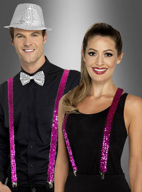 Ein Mann in Schwarz mit einem silbernen Paillettenhut und einer Fliege steht neben einer Frau in Schwarz; beide tragen die „Pailletten Hosenträger“ in Rosa – perfekte Fasching-Accessoires – vor einem grauen Hintergrund mit Farbverlauf.