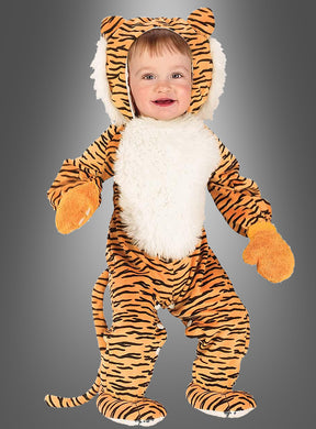 Ein kleines Kind, das das Tigerkostüm für Babys mit Handschuhen trägt – mit orange-schwarzen Streifen, einer weißen, pelzigen Brust, orangefarbenen Fäustlingen, einer Plüschmähne und einem Schwanz –, steht vor einem schlichten grauen Hintergrund.