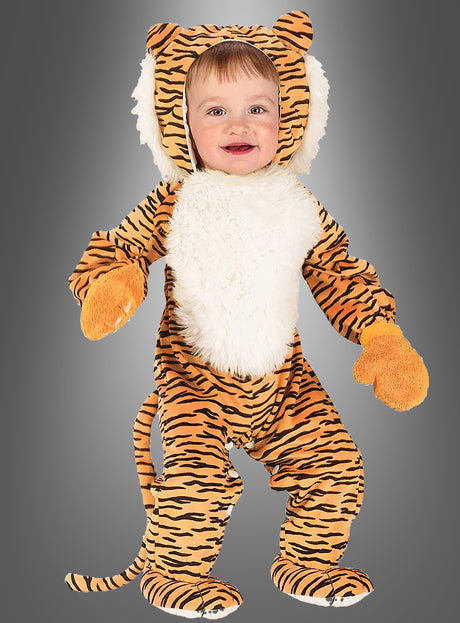Ein kleines Kind, das das Tigerkostüm für Babys mit Handschuhen trägt – mit orange-schwarzen Streifen, einer weißen, pelzigen Brust, orangefarbenen Fäustlingen, einer Plüschmähne und einem Schwanz –, steht vor einem schlichten grauen Hintergrund.