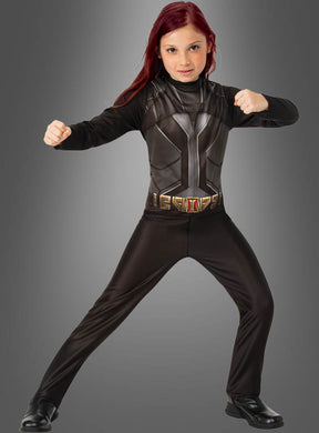 Ein rothaariges Kind in einem Superheldenkostüm – es trägt das Marvel Black Widow-Kostüm für Kinder – posiert mit angewinkelten Armen und erhobenen Fäusten sowie gespreizten Beinen vor einem grauen Hintergrund mit Farbverlauf.