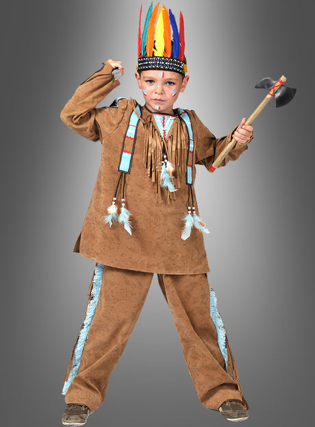 Ein Kind, das das „Kleiner Häuptling“-Indianerkostüm in Beige mit Wildleder-Optik, einen Federkopfschmuck und Gesichtsbemalung trägt, steht vor einem grauen Hintergrund und hält einen Spielzeug-Tomahawk in der Hand.