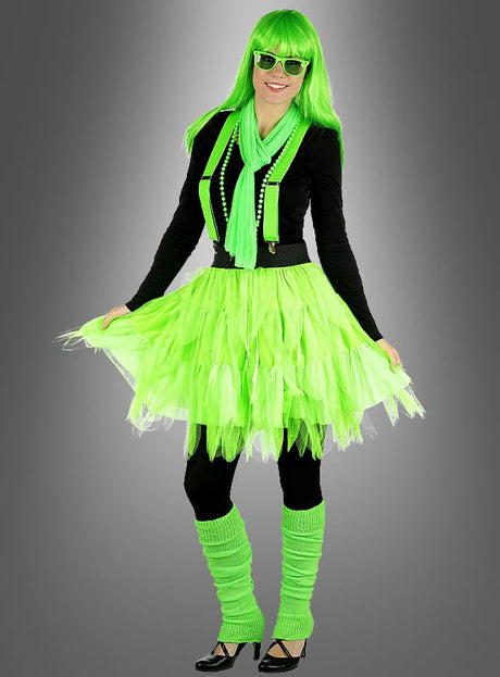 Diese Person trägt die „Glamour Leucht“-Perücke in Neonfarben, dazu eine auffällige Sonnenbrille, einen Schal, bunte Perlen, einen Tutu-Rock, Stulpen und Hosenträger über schwarzer Kleidung und steht lächelnd vor einem grauen Hintergrund mit Farbverlauf – ein Bild, das den energiegeladenen Geist einer 80er-Jahre-Party perfekt einfängt.