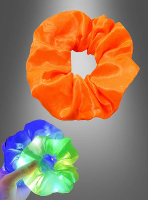 Ein orangefarbenes Scrunchie-Haargummi mit LED ist über einer Hand abgebildet, die das leuchtende Scrunchie hält, das vor einem grauen Hintergrund mit blauen, grünen und weißen LEDs leuchtet – ein echter Blickfang unter den leuchtenden Haarschmuckstücken.