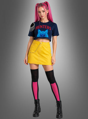 Eine Frau mit rosa Haaren in Zöpfen trägt das „K-Pop Hunters Mari“-Outfit für Damen – bestehend aus einem marineblauen Crop-Top, einem gelben Rock mit Kette, schwarzen Stiefeln sowie schwarzen und rosa Overknee-Socken – und posiert vor einem grauen Hintergrund, was einen auffälligen, von K-Pop-Sängerinnen inspirierten Look ergibt.