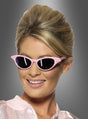 Eine lächelnde Frau mit einer Beehive-Frisur trägt die „Vintage Sonnenbrille 50er Jahre rosa“ – eine retro-rosa Cat-Eye-Sonnenbrille, die mit Strasssteinen verziert ist – sowie ein hellrosa Hemd mit Kragen. Vor einem grauen Hintergrund mit Farbverlauf vermittelt das Bild das authentische Flair der 50er Jahre.
