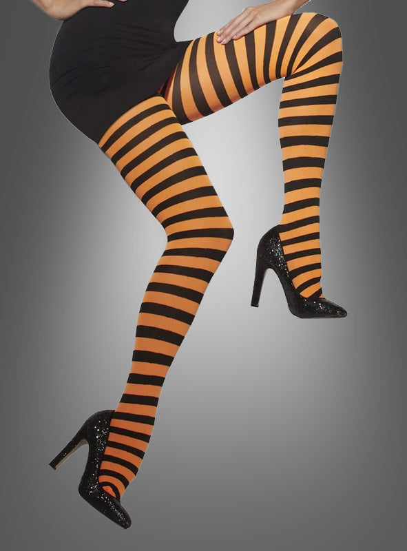 Die Person trägt orange-schwarze Ringel-Strumpfhosen für Damen und schwarze High Heels und posiert mit einem angewinkelten und einem ausgestreckten Bein vor einem grauen Hintergrund mit Farbverlauf, wodurch ein auffälliger Karnevalskostüm-Look entsteht.