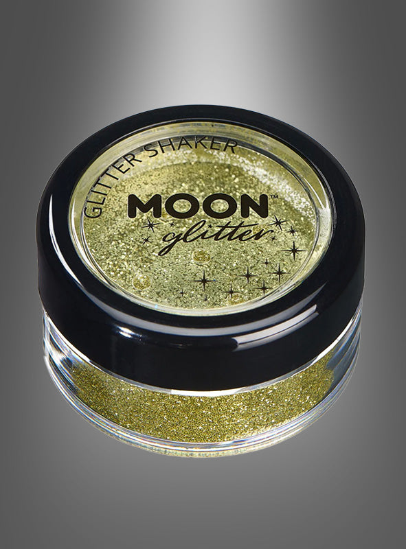 Ein kleines, rundes Töpfchen mit 5 g losem Glitzerpuder in Gold, gefüllt mit goldenem Glitzer und verschlossen mit einem schwarzen Deckel mit der Aufschrift „Moon Glitter“, wird vor einem dunkelgrauen Hintergrund mit Farbverlauf präsentiert – der perfekte Glitzer für Gesicht und Körper.