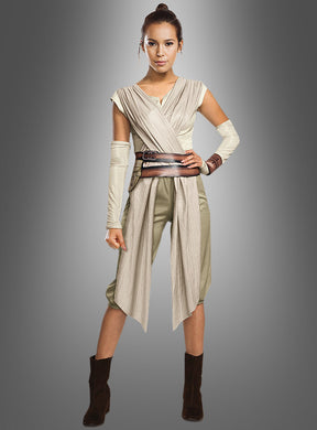Vor einem grauen Hintergrund mit Farbverlauf steht eine Frau selbstbewusst da, gekleidet im „STAR WARS Episode 7 Rey Kostüm Deluxe“ – einem beige-braunen, von Science-Fiction inspirierten Ensemble mit Armwickeln, einem Gürtel in der Taille, einer kurzen Hose und Stiefeln. Dieser Look ist perfekt für Ihren nächsten Auftritt in Ihrem Star Wars-Damenkostüm.