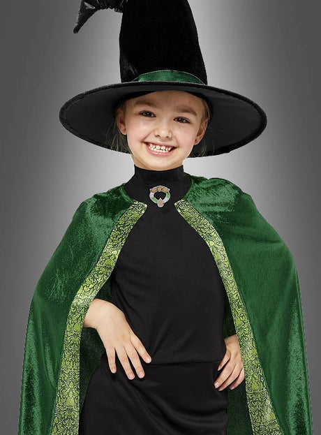 Ein junges Mädchen lächelt, es trägt einen schwarzen Hexenhut und einen grünen Samtumhang mit goldener Borte über einem schwarzen Shirt und verkörpert damit perfekt den magischen Geist des Professor-McGonagall-Kostüms für Kinder.